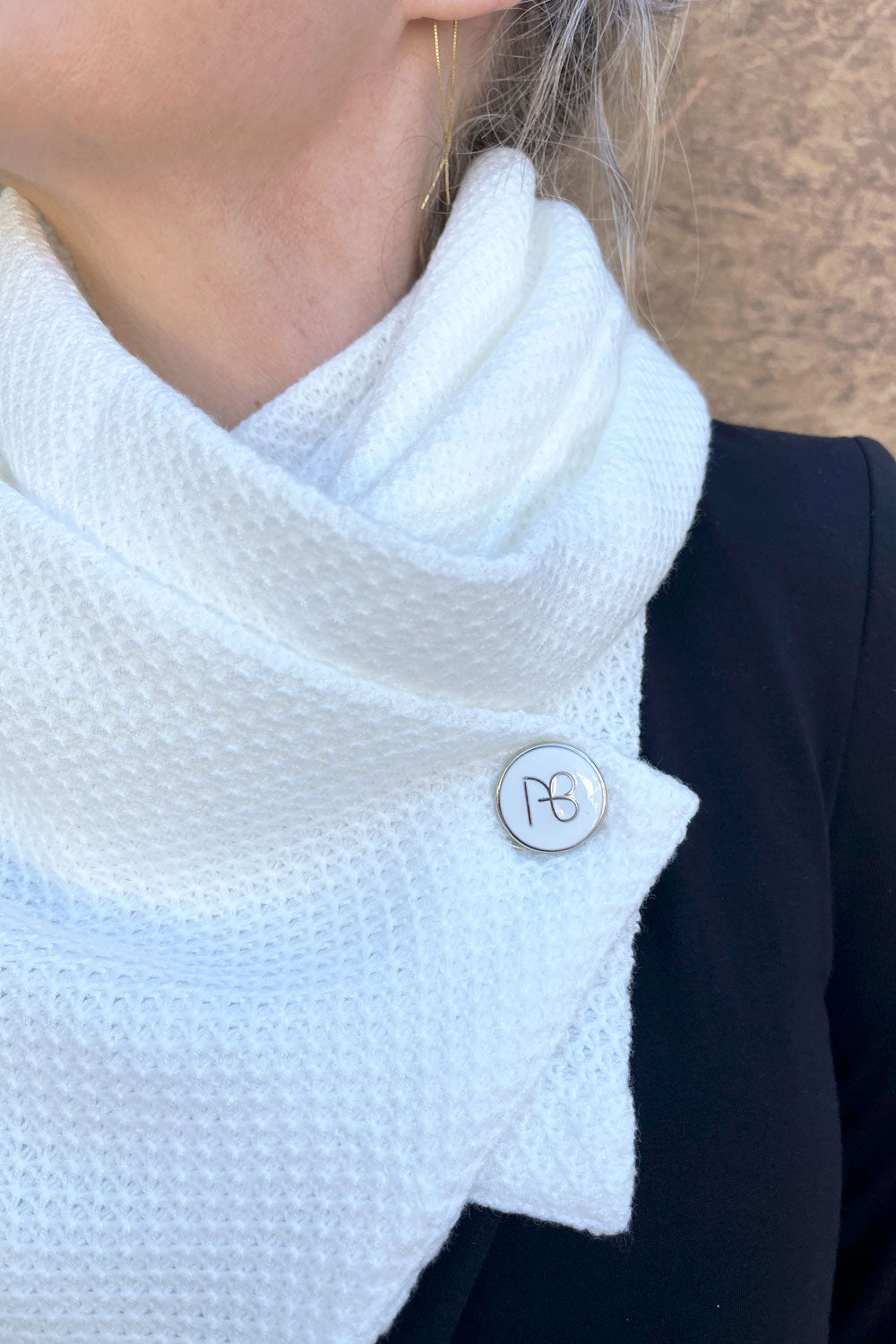 צעיף סרוג שֵינָה בצבע שמנת עם טקסטורת מעוינים וכפתור אמייל לבן זהוב